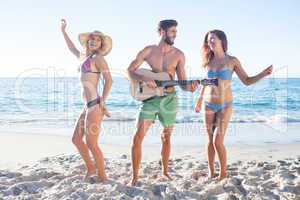 Handsome man playing guitar and his friends dancing