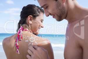 Handsome man putting sun tan lotion on his girlfriend
