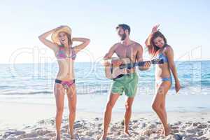 Handsome man playing guitar and his friends dancing