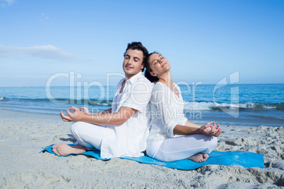 Happy couple doing yoga beside the water