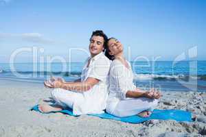 Happy couple doing yoga beside the water