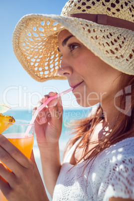 Brunette wearing straw hat and drinking a cocktail