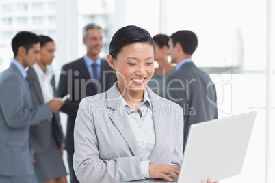 Businesswoman using laptop with colleagues behind