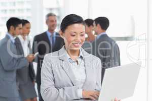 Businesswoman using laptop with colleagues behind