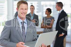 Businessman working on laptop with colleagues behind him