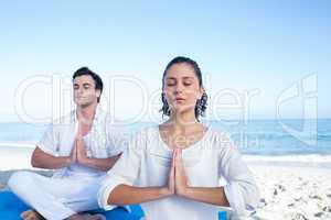 Happy couple doing yoga beside the water