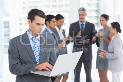 Businessman using laptop with colleagues behind