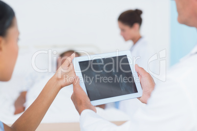 Doctor using digital tablet with colleagues and patient behind