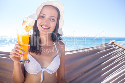 Smiling brunette relaxing on the hammock and holding a cocktail