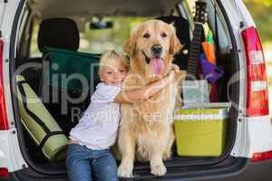 Smiling little girl with her dog in car trunk