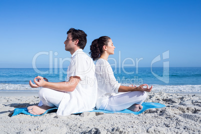 Happy couple doing yoga beside the water