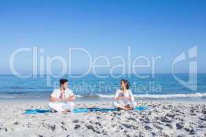 Happy couple doing yoga beside the water