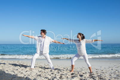 Happy couple doing yoga beside the water