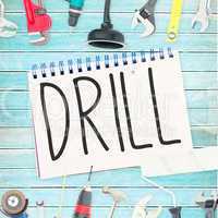 Drill against tools and notepad on wooden background