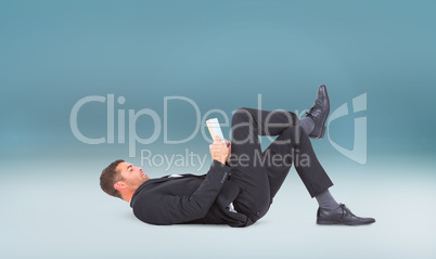 Composite image of businessman lying on the floor reading book