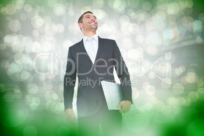 Composite image of businessman looking up holding laptop