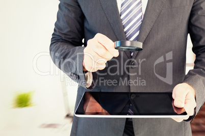 Composite image of businessman looking at tablet with magnifying