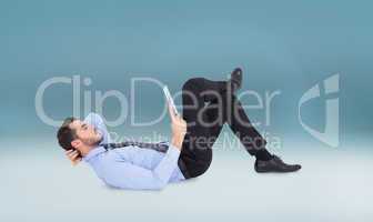 Composite image of businessman lying on floor using tablet