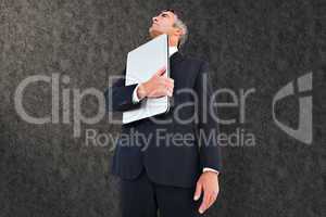 Composite image of businessman in suit holding his laptop proudl