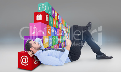 Composite image of businessman lying on floor using tablet