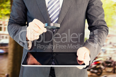 Composite image of businessman looking at tablet with magnifying Composite image of businessman looking at tablet with magnifying