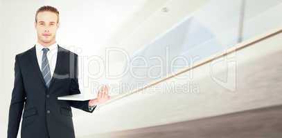 Composite image of serious businessman posing and holding laptop
