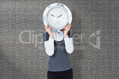 Composite image of woman holding clock in front of her head