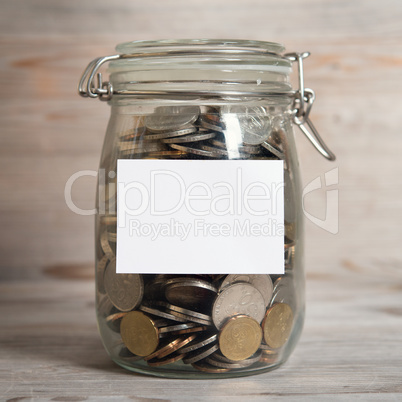 Coins in glass money jar with white blank label