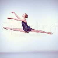Beautiful young ballet dancer jumping on a gray background.
