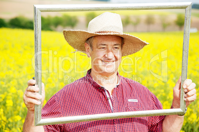 Farmer with photo frame is placed in canola field