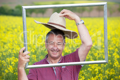 Farmer with photo frame is placed in canola field
