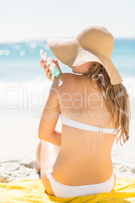 Pretty blonde woman putting sun tan lotion on her shoulder