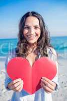 Smiling woman holding heart card at the beach