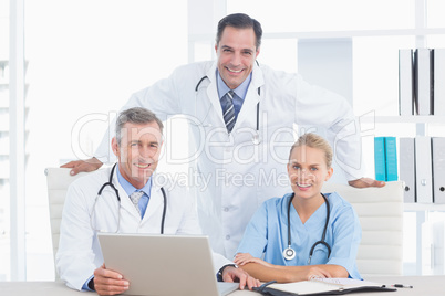 Smiling doctors and nurse looking at camera in front of laptop Smiling doctors and nurse looking at camera in front of laptop