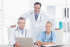 Smiling doctors and nurse looking at camera in front of laptop