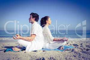 Happy couple doing yoga beside the water