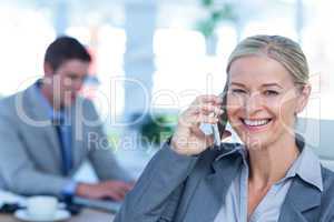 Smiling businesswoman having a phone call with colleague in back