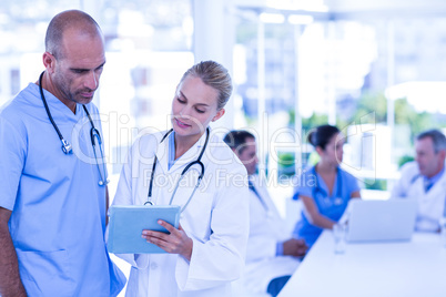 Two doctors looking at clipboard while their colleagues working