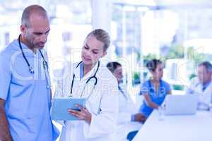 Two doctors looking at clipboard while their colleagues working