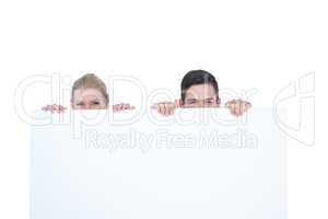 Young couple hiding behind a blank sign