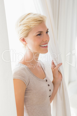 Pretty smiling blonde woman holding curtain