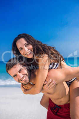 Man giving piggy back to his girlfriend at the beach