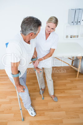 Doctor helping her patient walking with crutch