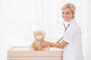 Smiling blonde doctor with stethoscope in the teddy bear