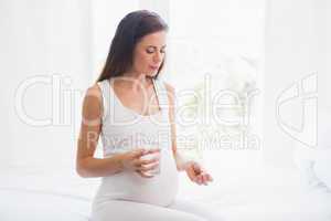 Pregnancy sitting on the bed taking a vitamin