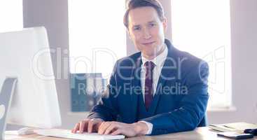 Smiling businessman typing on laptop and looking at camera