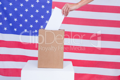 Hand putting ballot in vote box behind american flag