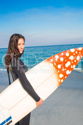 Woman in wetsuit with a surfboard on a sunny day