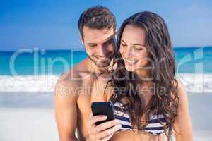 Happy couple using smartphone at the beach