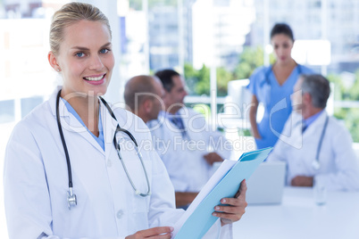 Smiling female doctor looking at camera while her colleages work